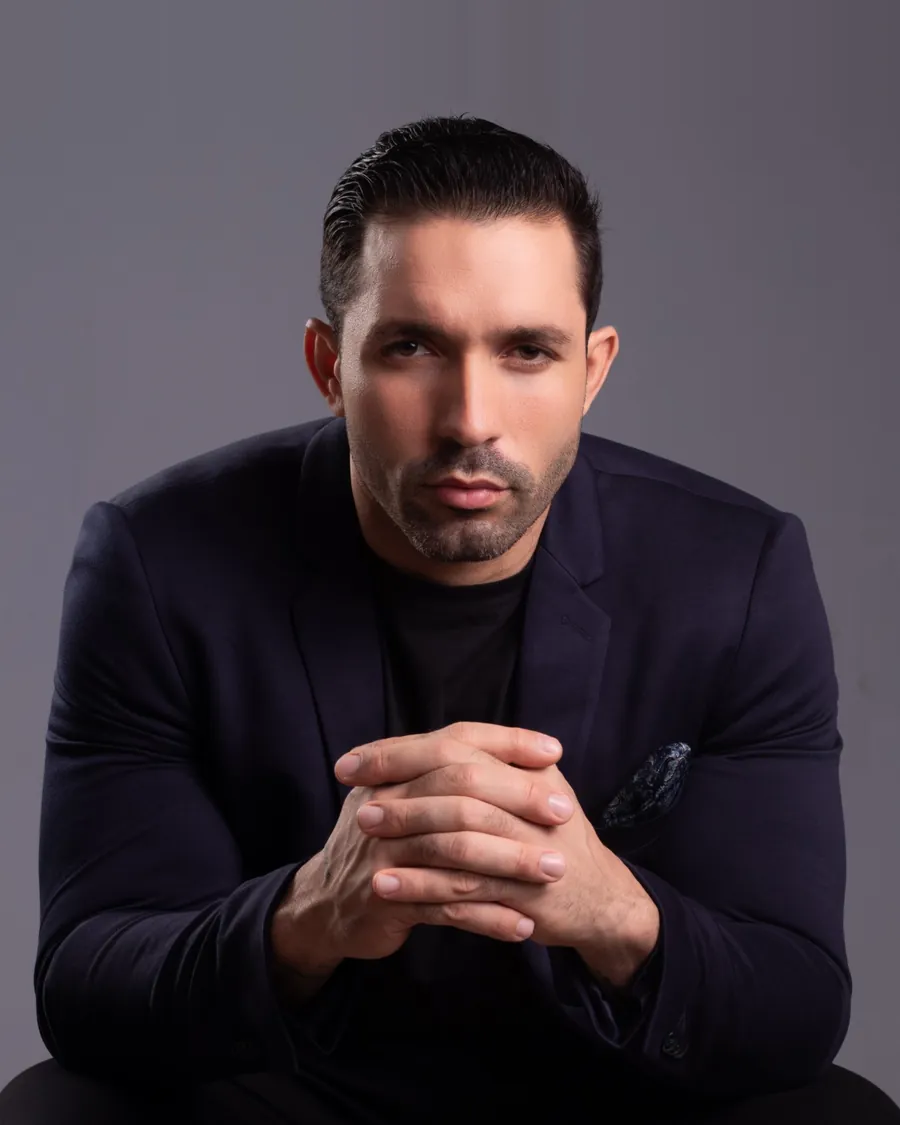 Lucas Reis, fundador da Levon Clothing e embaixador da ConneIA, de blazer azul-marinho e mãos entrelaçadas, em retrato de estúdio